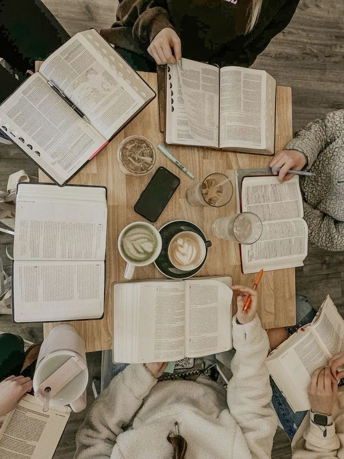 Group of people studying at a table with open books, coffee cups, and stationery.